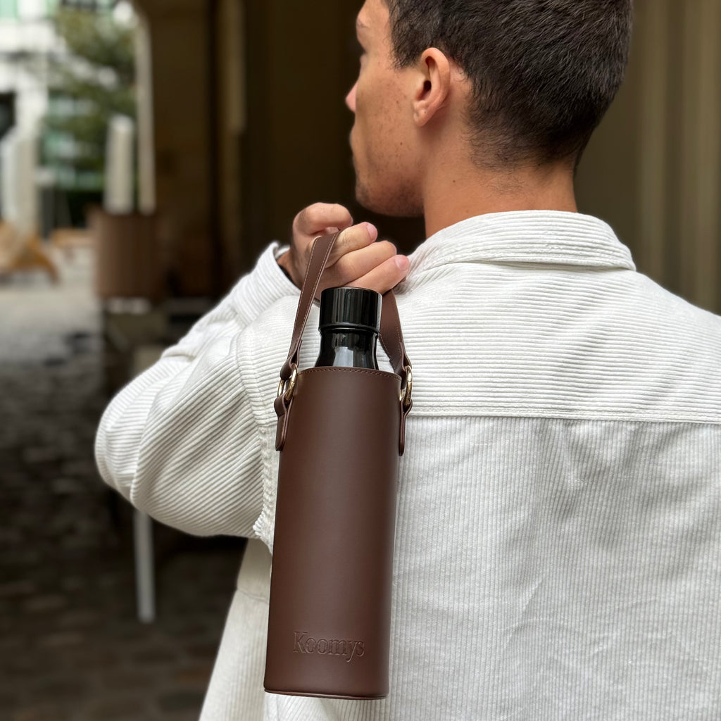 Porte-gourde en cuir vegan marron KOOMYS porté à l’épaule pour transporter une bouteille