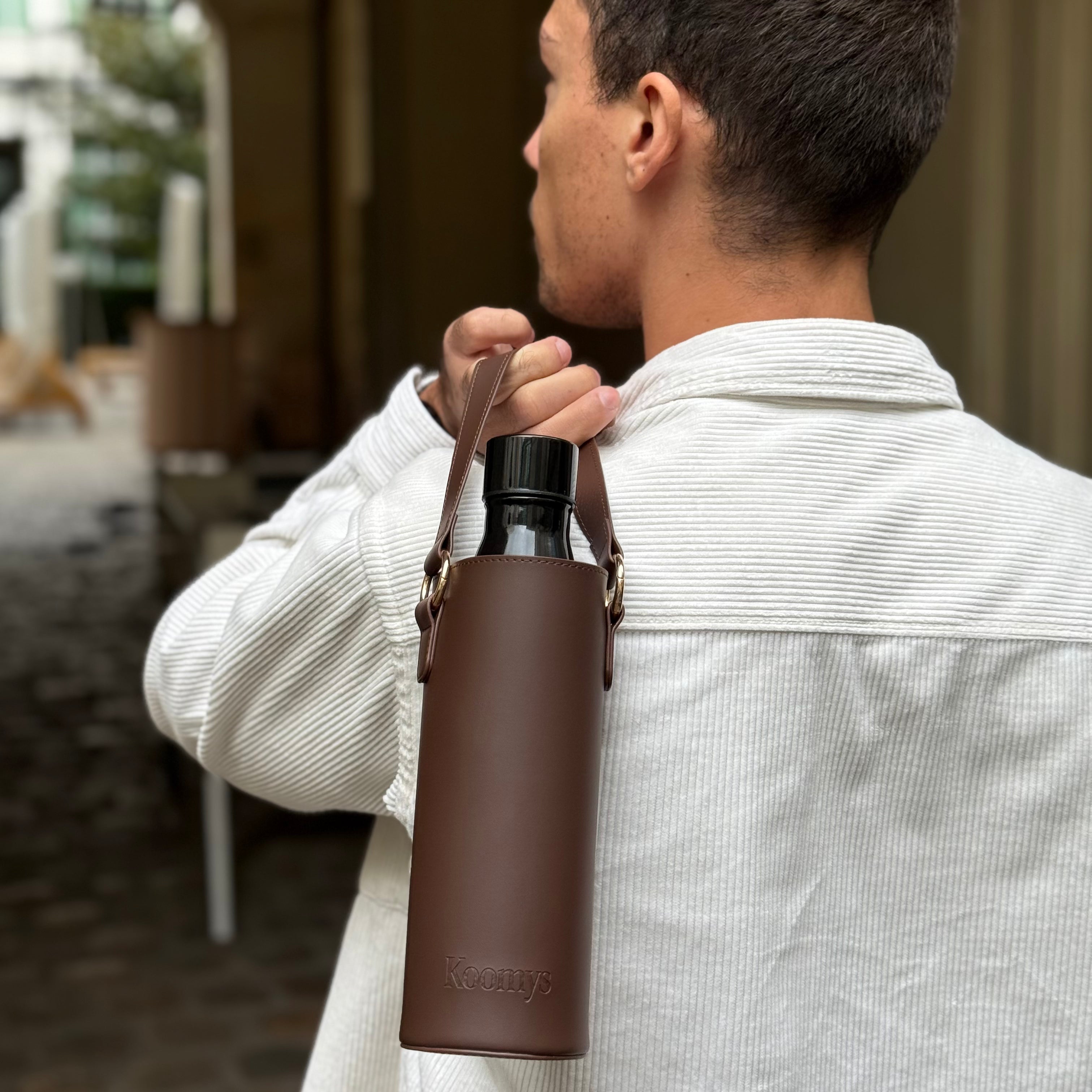 Porte-gourde en cuir vegan marron KOOMYS porté à l’épaule pour transporter une bouteille