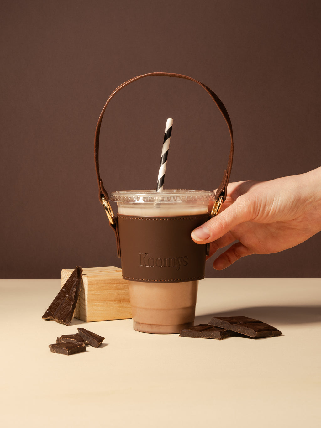 Main tenant un porte-gobelet KOOMYS en cuir vegan marron avec boisson