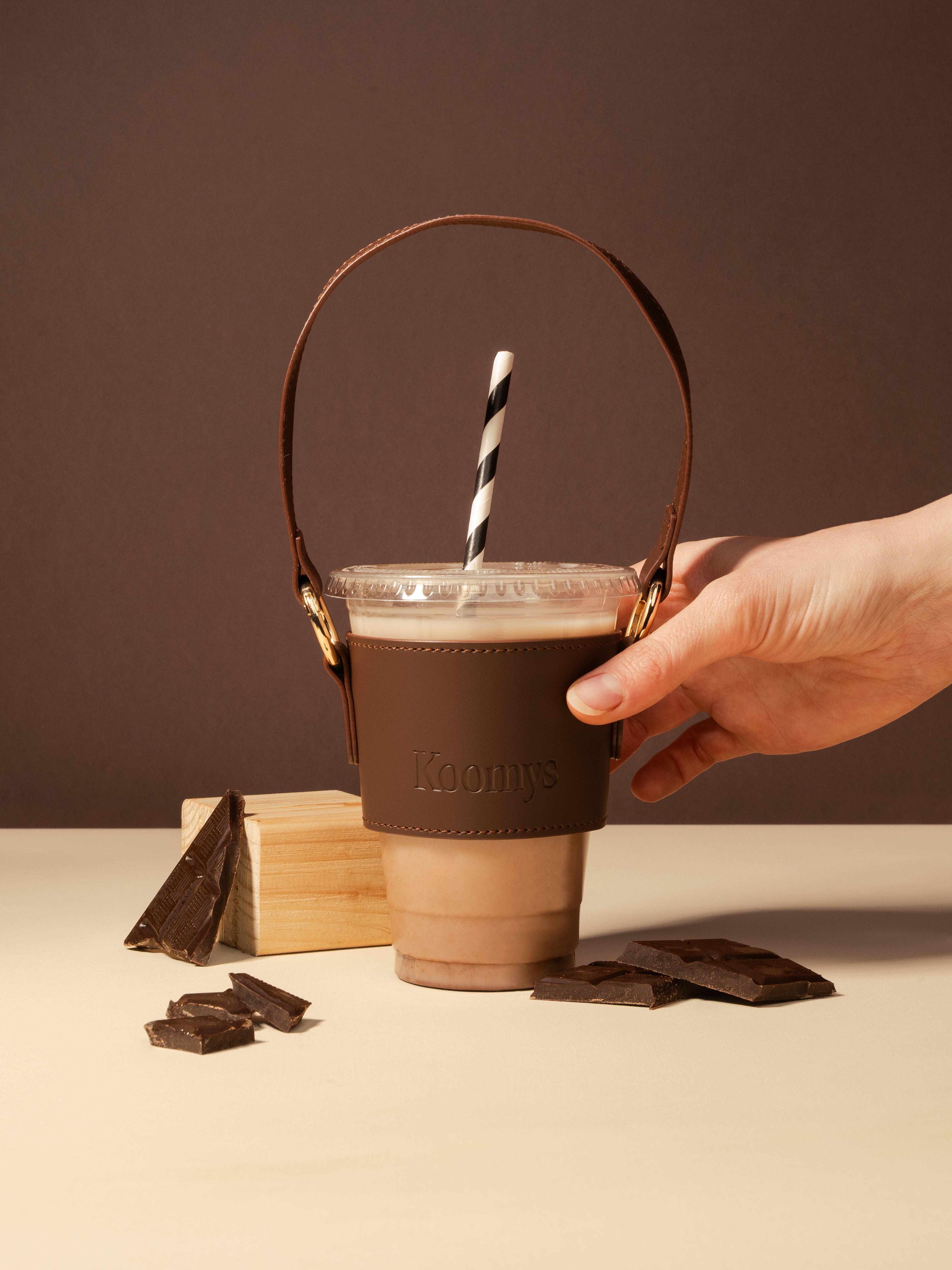 Main tenant un porte-gobelet KOOMYS en cuir vegan marron avec boisson